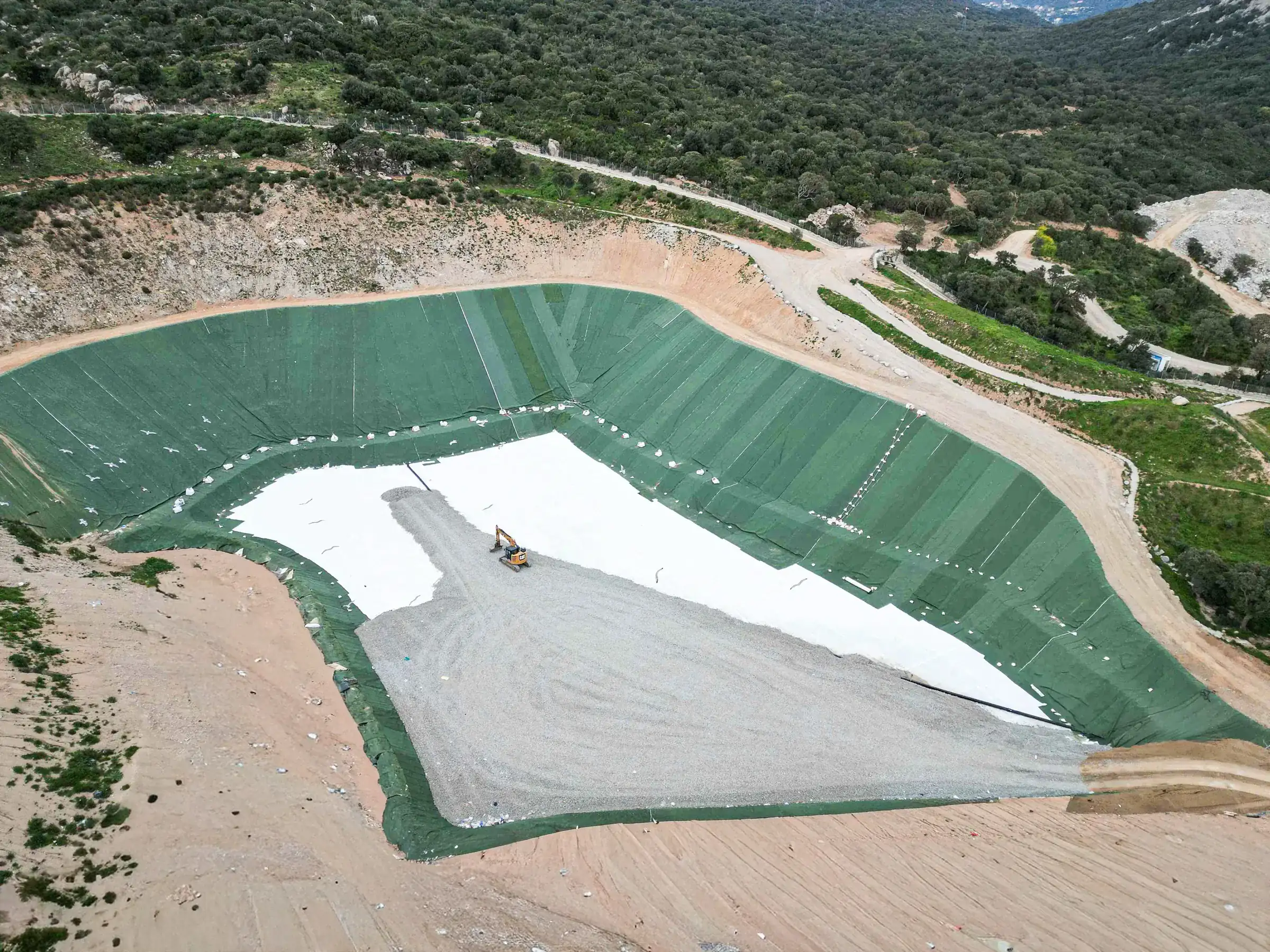 Vue aérienne du casier de stockage en construction — géomembrane verte, géotextile blanc, pelle mécanique